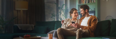 two people sitting together on a couch reviewing tax filing options on a smartphone, representing H&R Block’s user-friendly experience compared to TurboTax