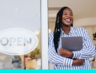 A small business owner smiling standing in a doorway to a business